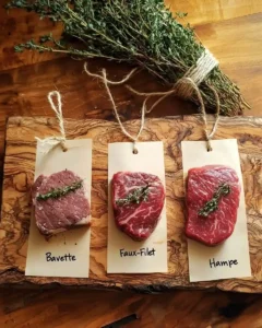Planche en bois avec trois pièces de bœuf – faux-filet, bavette et hampe – présentées côte à côte avec des étiquettes manuscrites