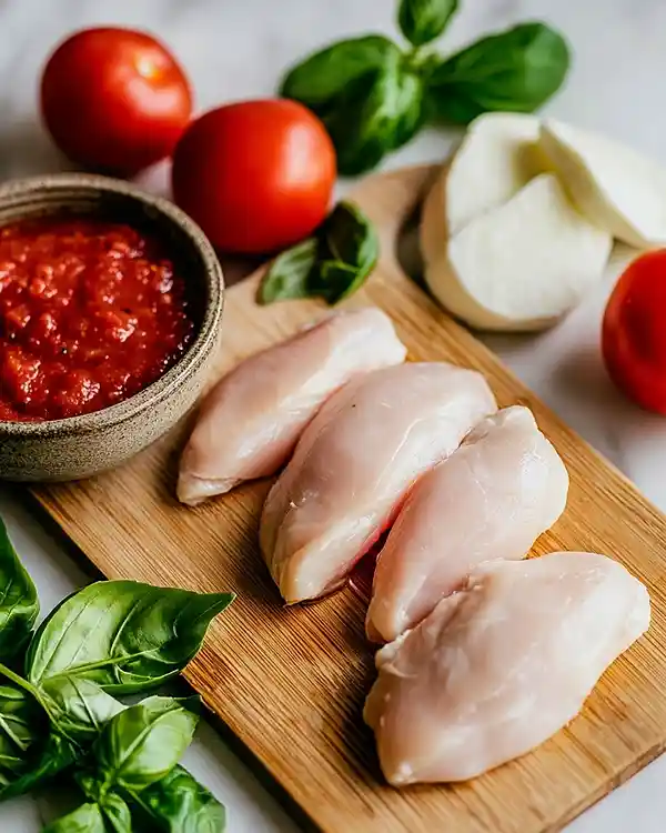 Recettes Poulet à l'Italienne 2 Préparation du poulet à l'italienne avec filets de poulet, sauce tomate maison, basilic frais et mozzarella sur planche de bois
